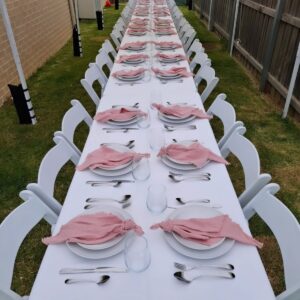 Long table set with plates, stainless steel cutlery, glassware and pink napkins