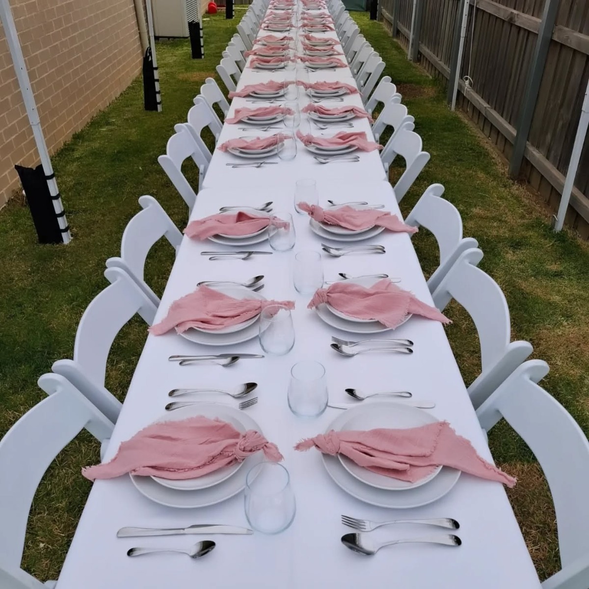 Long table set with plates, stainless steel cutlery, glassware and pink napkins