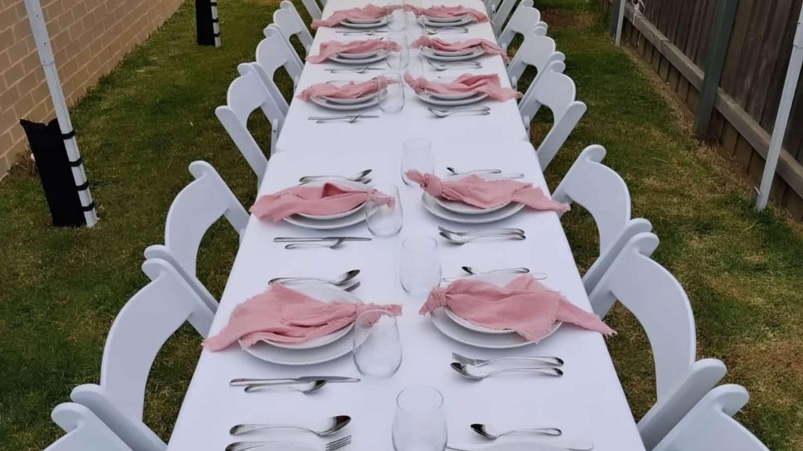 Long table set with white linen, dinnerware and chairs by JK Party Hire