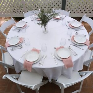 Round banquet table dressed in white linen with place settings and pink napkins